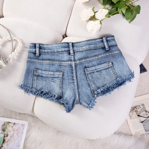 Flachbild von hellblauen Jeans-Shorts mit ausgefransten Kanten auf weißem Ledersofa