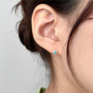 Close-up of heart-shaped blue zircon stud earrings in 925 sterling silver on a woman's ear