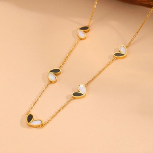 Close-up of gold chain necklace featuring five black and white enamel heart pendants