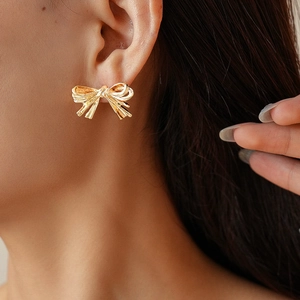Detailed close-up of golden metallic bow earring with textured ribbon folds on earlobe