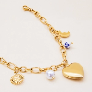 Close-up of gold charm bracelet featuring heart, sun, and porcelain bead details