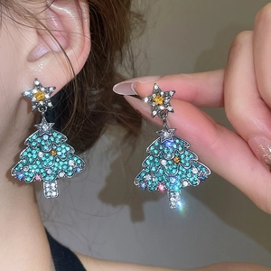 Détail de boucles d'oreilles sapin de Noël avec strass bleus et étoile sur le modèle