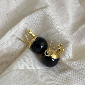 Detail of gold 925 silver earrings with polished black agate beads on linen fabric