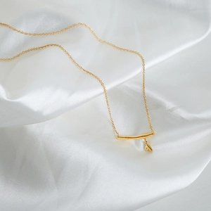 Collier style bambou plaqué or 18k avec pendentif feuille sur fond de soie blanche