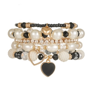 Dettaglio di bracciali a strati con perline e ciondoli a cuore in nero, bianco e oro