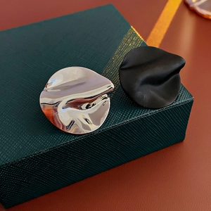 Detail of asymmetric silver and black metallic stud earrings on a luxury green gift box
