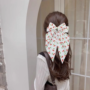 Detail of large white bow hair clip with cherry print on model's hairstyle