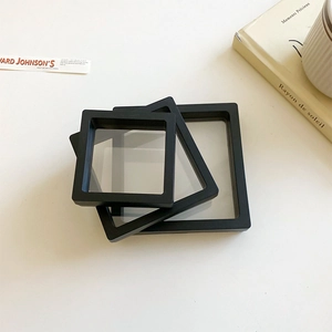 Three black square PE film floating frames for jewelry display on a minimalist white desk