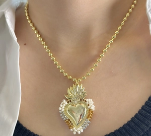 Detail of beaded sacred heart pendant with gold finish on a delicate beaded chain necklace