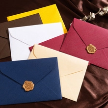 Artistic stack of colorful kraft envelopes with decorative gold wax seals and dried leaves