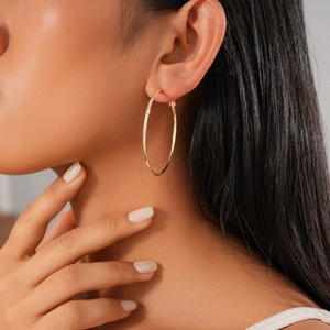 Close-up of a model wearing high-shine gold hoop earrings in a minimalist round design