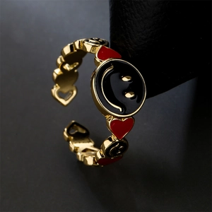 Funny gold plated smiley face and red heart open ring on dark textured background