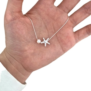 Elegant silver starfish necklace with pearl accent shown on hand for size reference