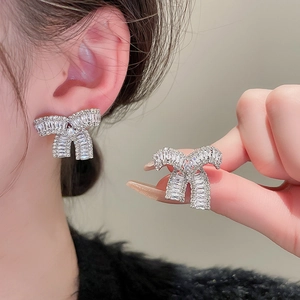 Elegant bow-shaped silver stud earrings with sparkling cubic zirconia on a model