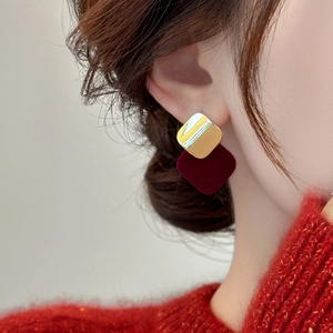 Detail view of a model wearing square velvet earrings with gold finish and deep red flocking