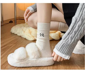 Detail of cream rib-knit mid-tube socks featuring black embroidered bow and plush slippers