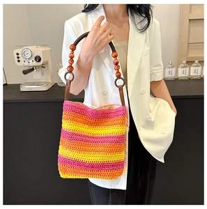 Detail of rainbow gradient straw bag with handcrafted wooden bead handle on shoulder