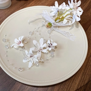 Detail of floral hair clip featuring white fabric petals, pearls and lace ribbons