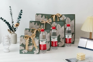 Green paper gift bags with white floral patterns and gold ribbon handles in four sizes