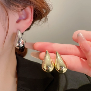 Detailed close-up of large metallic teardrop earrings in polished gold and silver finishes