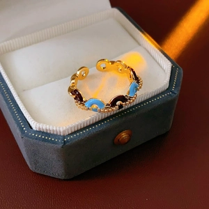 Dettaglio di un anello regolabile dorato con smalto blu e marrone su scatola di velluto