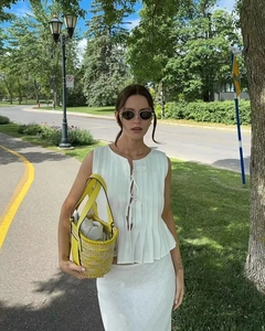 Detail of white pleated sleeveless top with tie neck and yellow woven bucket bag
