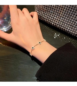 Detailed macro of gold flower bracelet with emerald stones and pearls on wrist
