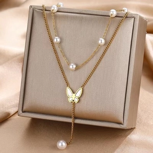 Detail of double-layer golden necklace with white pearl accents and butterfly pendant
