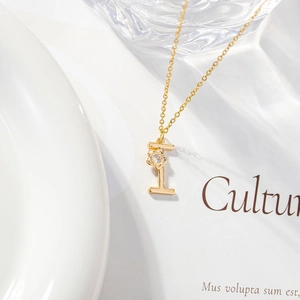 Detail of gold letter I pendant necklace with zircon stone on white background