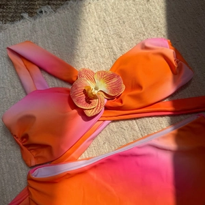 Détail d'un bikini dégradé rose-orange avec une fleur d'orchidée sur le haut bandeau