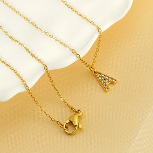 Collier doré en acier inoxydable avec pendentif lettre A en strass sur une assiette blanche