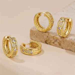 Détails de créoles dorées avec cristaux blancs ronds et losanges sur fond de pierre