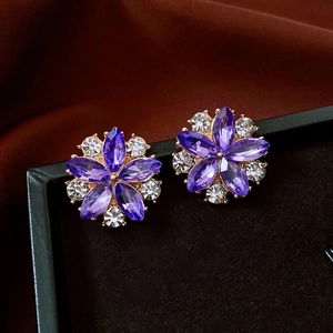 Macro shot of purple crystal flower earrings on a black cushion with golden metal base