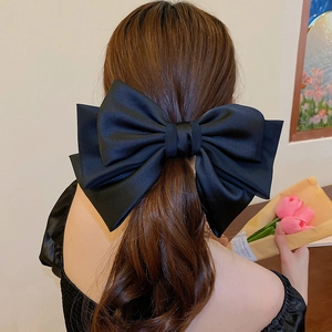 Detail of an oversized black satin bow hair clip styled on hair for an elegant look