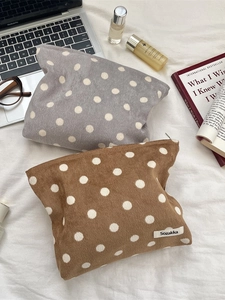 Polka dot corduroy cosmetic bags in brown and grey, organized on a soft fabric backdrop