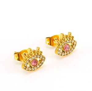 Detailed macro shot of gold devil eye stud earrings with pink stone and white crystals