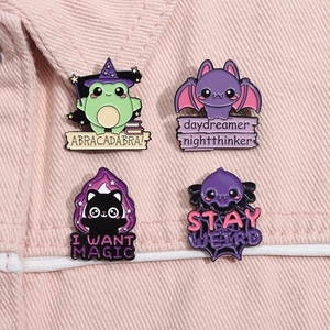 Detail of four cartoon enamel pins with cat and bat motifs on pink denim fabric