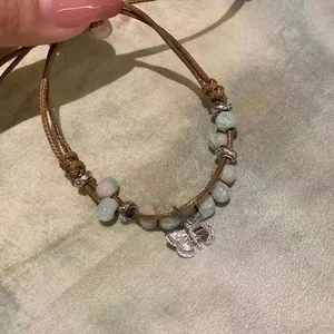 Detail of hand-woven bracelet with mixed color beads and silver butterfly charm