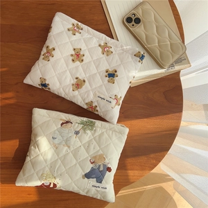 Flat lay of a quilted cream makeup bag with cute bear and rabbit prints on a wood table