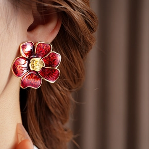 Primer plano de pendientes vintage de flores rojas con bordes dorados en una modelo