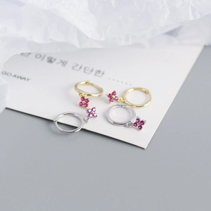 Detail of silver and gold flower earrings with red stones on a minimalist background