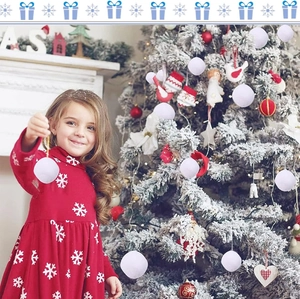 Little girl holding soft white snowball ornaments in front of a decorated Christmas tree