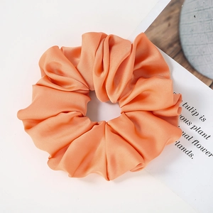 Detailed view of large orange satin scrunchie with rich pleated texture and soft silk sheen