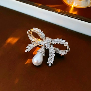 Broche nœud argentée avec cristaux et perle pendante sur fond de bois sombre luxueux