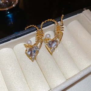 Close-up of C-shaped heart earrings with rhinestones, pearls and golden twisted metal