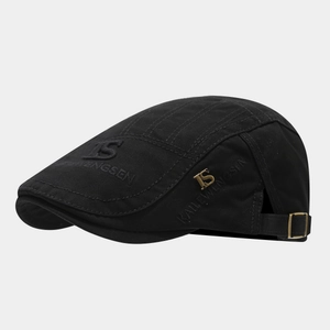 Close-up of black retro flat cap with gold metal logo and detailed embroidery
