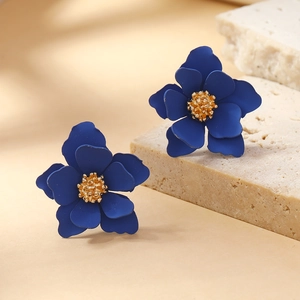 Macro detail of dark blue matte petal earrings with golden textured centers on stone
