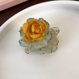 Close-up of a gradient yellow camellia flower hair clip with green silk fabric leaves