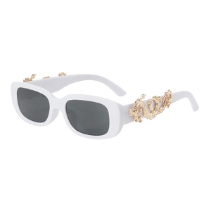 Close-up of golden dragon emblem on white oval sunglasses with dark lenses