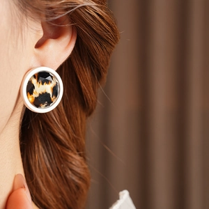 Close-up of a faceted round leopard print earring with a white border on a model ear